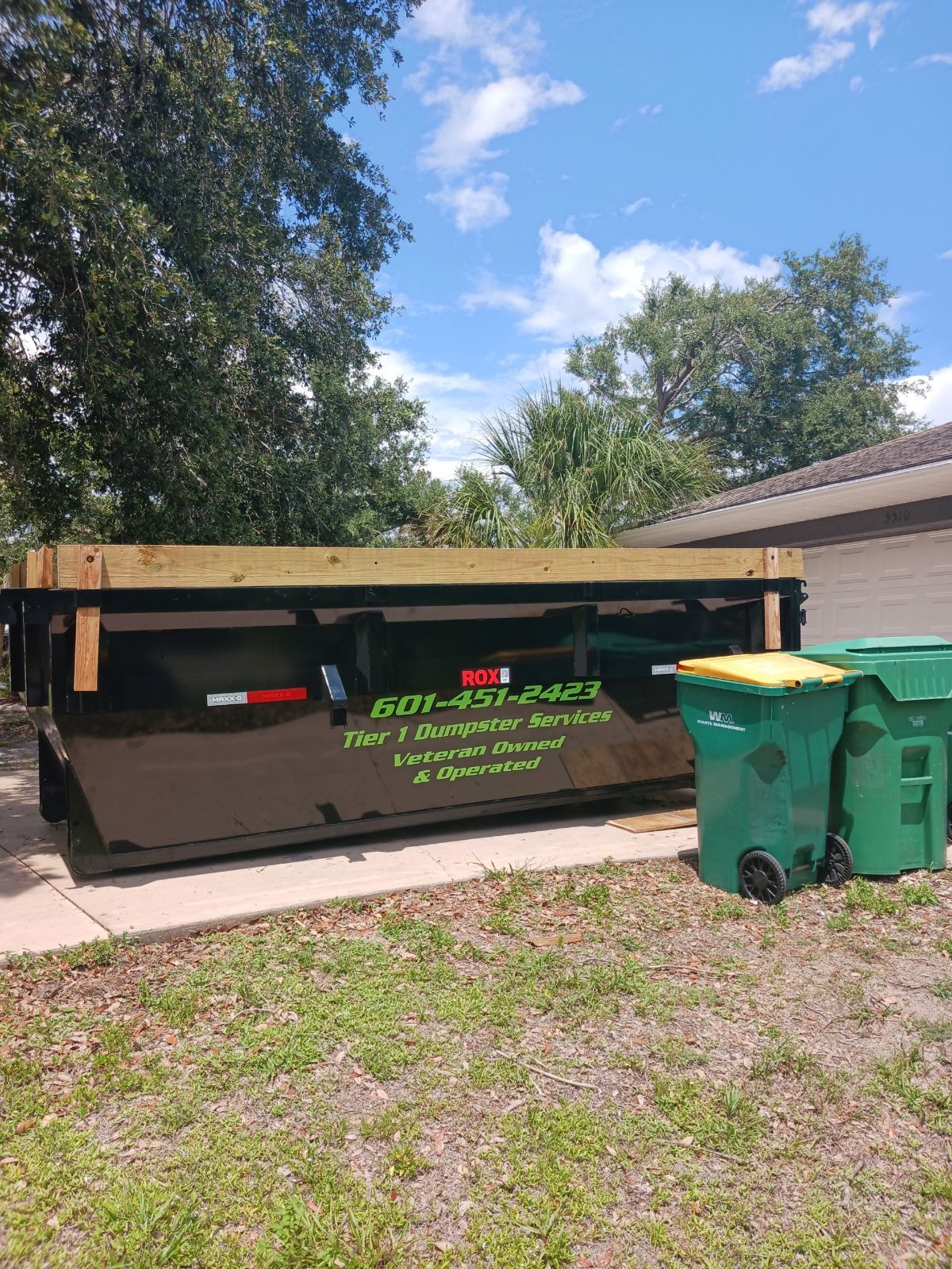 Dumpster rental dropped off on a concrete driveway outside of a house in Lehigh Acres FL